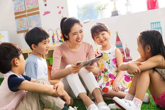 A warm Singaporean preschool classroom with an educator reading to young children